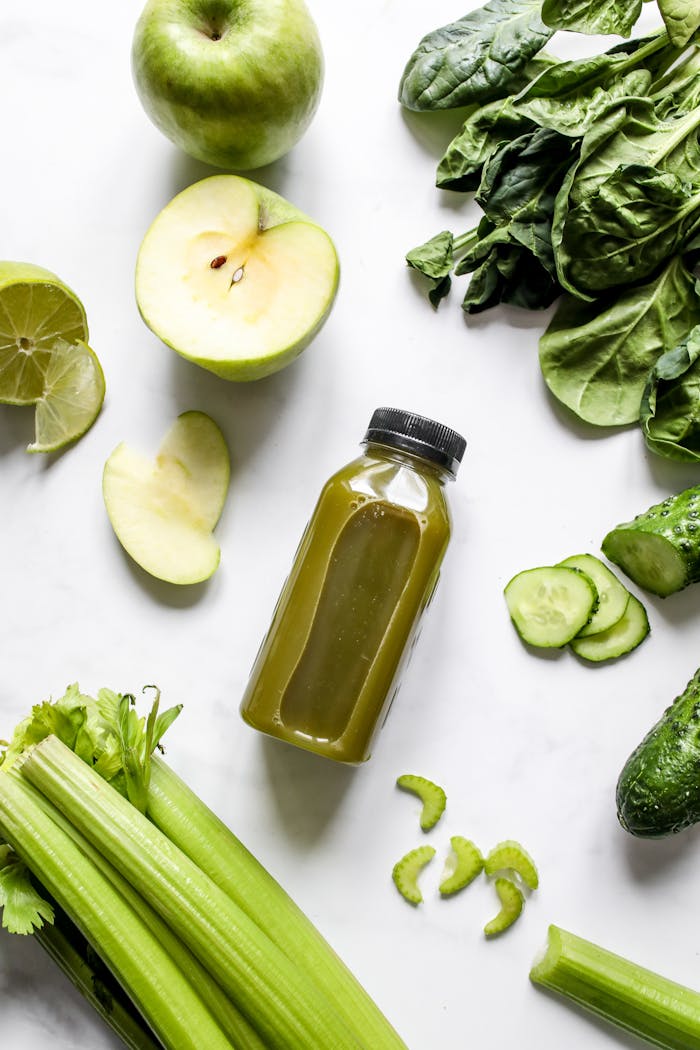 Flatlay of fresh green juice with vegetables and fruits on a white background, perfect for healthy lifestyle concepts.
